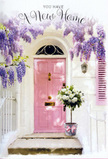The doorway in this scene looks like a quiet corner of Cobham on a gentle afternoon, perfectly staged to celebrate someone's arrival in a new home. At its centre stands a pastel pink front door, the kind of soft, powdery rose shade that feels instantly welcoming, bordered by a whitewashed wall whose subtle texture adds character without distraction. A single painted shutter, tilted open to one side, repeats the same blush tone and frames the composition with understated charm. From above, wisteria trails down in generous, layered curtains of lilac and lavender blossoms, their clusters dense and pendulous, creating an arch of colour that softens the architecture and hints at fragrance drifting through the air. The flowers hang in different lengths, some nearly grazing the pink door, others hovering above the step, so that the whole space feels cocooned in florals. At ground level, resting neatly on the stone doorstep, a simple grey metal bucket serves as a vessel for an abundant arrangement. This bucket is packed with white and cream roses, their velvety petals arranged so tightly that each bloom seems to nestle into the next, forming a plush, cloud-like mass of ivory and soft butter tones. Slender sprigs of green foliage weave between them, introducing freshness and structure without altering the calming palette. A narrow pink ribbon, matching the door, is tied around the bucket's base in a relaxed bow, its satin ends trailing lightly across the step. Soft daylight falls across the whole scene, seeping through the wisteria and creating gentle patches of light and shadow that move across the wall and flowers. The impression is of a housewarming gift delivered to a Cobham address near the meandering River Mole or the quiet roads leading to Fairmile, a floral moment that quietly says welcome home and carries with it all the tenderness and hope of a new beginning.